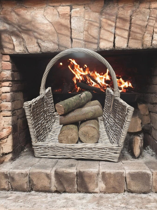 Greywash willow log basket filled with firewood placed in front of a burning fireplace