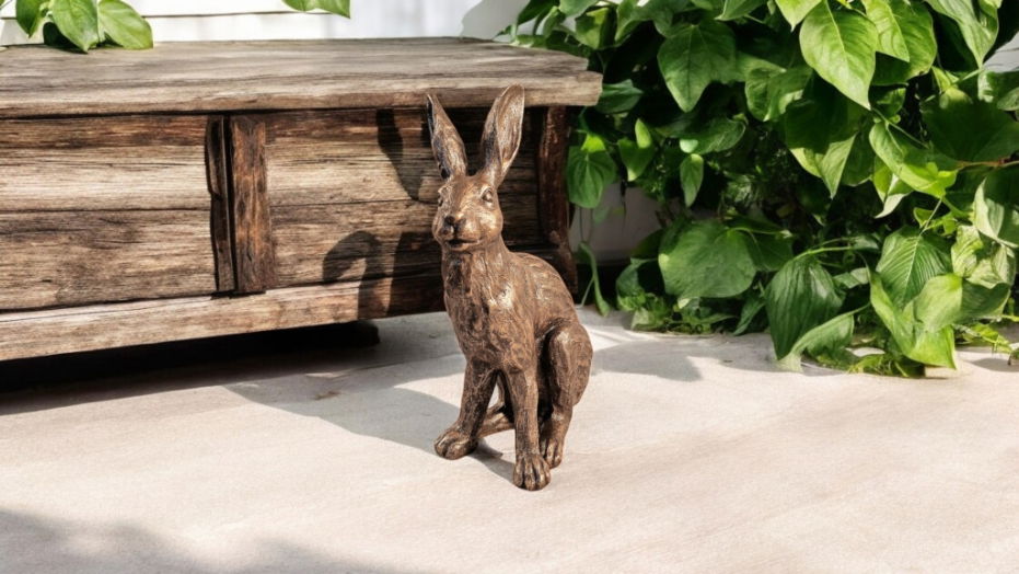 Hare brass ornament by Geko Products placed outdoors next to wooden furniture and green plants