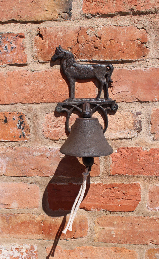 Rustic horse wall bell decor made of metal mounted on a brick wall with a rope pull