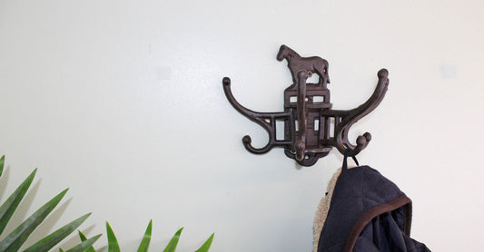 Geko Products cast iron horse coat hooks mounted on wall holding a blue coat near green plants