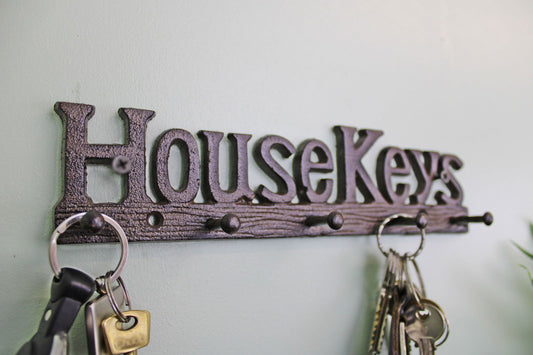 Rustic cast iron wall hooks in the shape of House Keys holding multiple key rings on a light wall