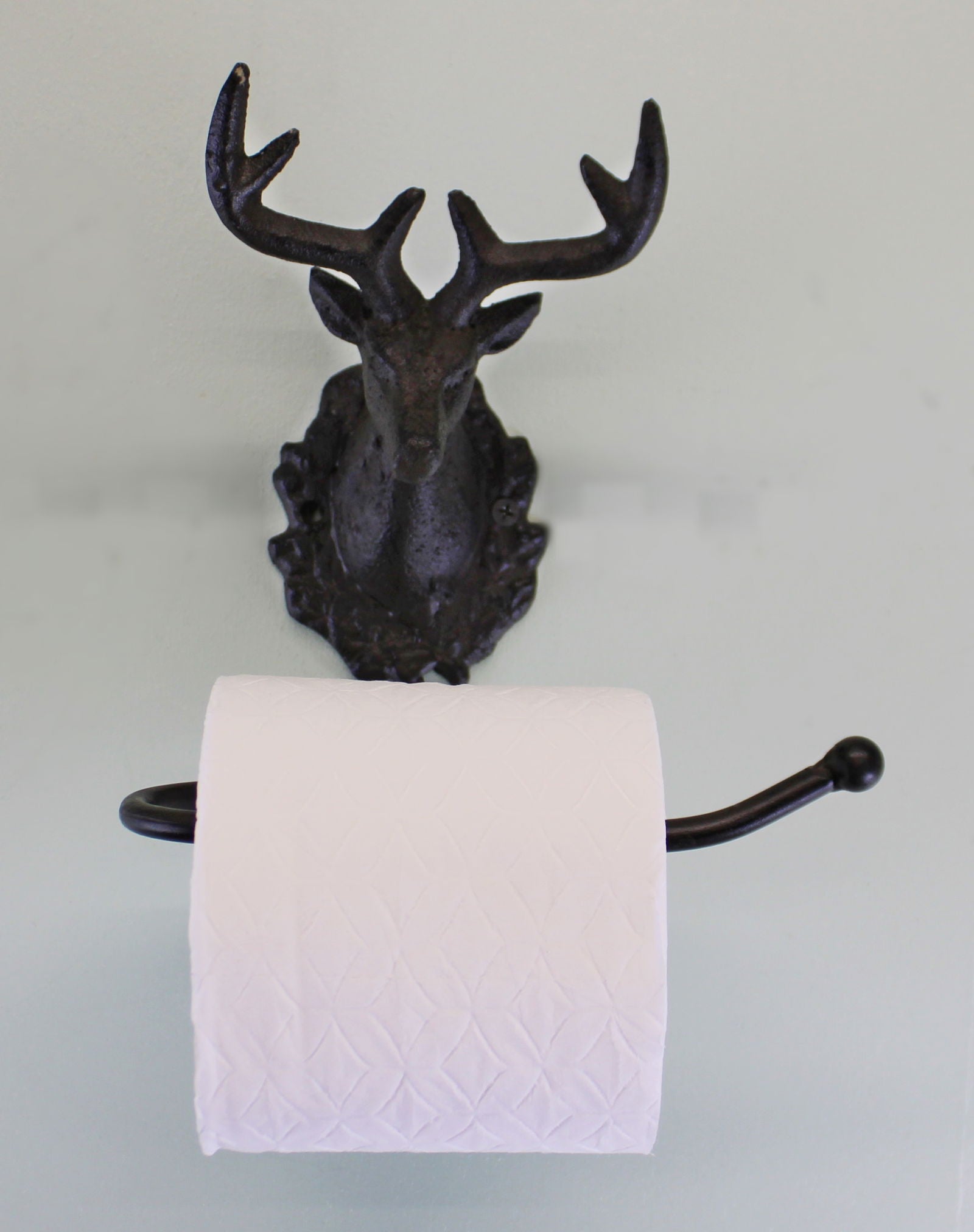 Rustic stag head toilet roll holder in dark metal mounted on wall holding white toilet paper roll