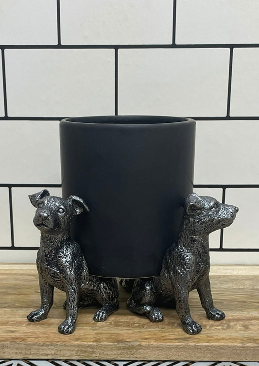 Silver dog pot risers featuring two detailed dog figurines supporting a black planter on wooden surface