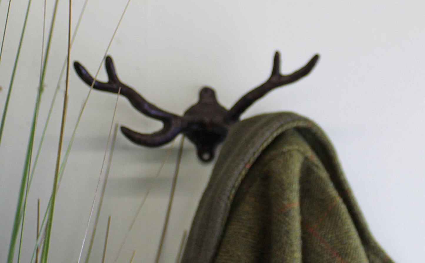 Geko Products stag antler wall mount in dark metal holding a green coat on a white wall