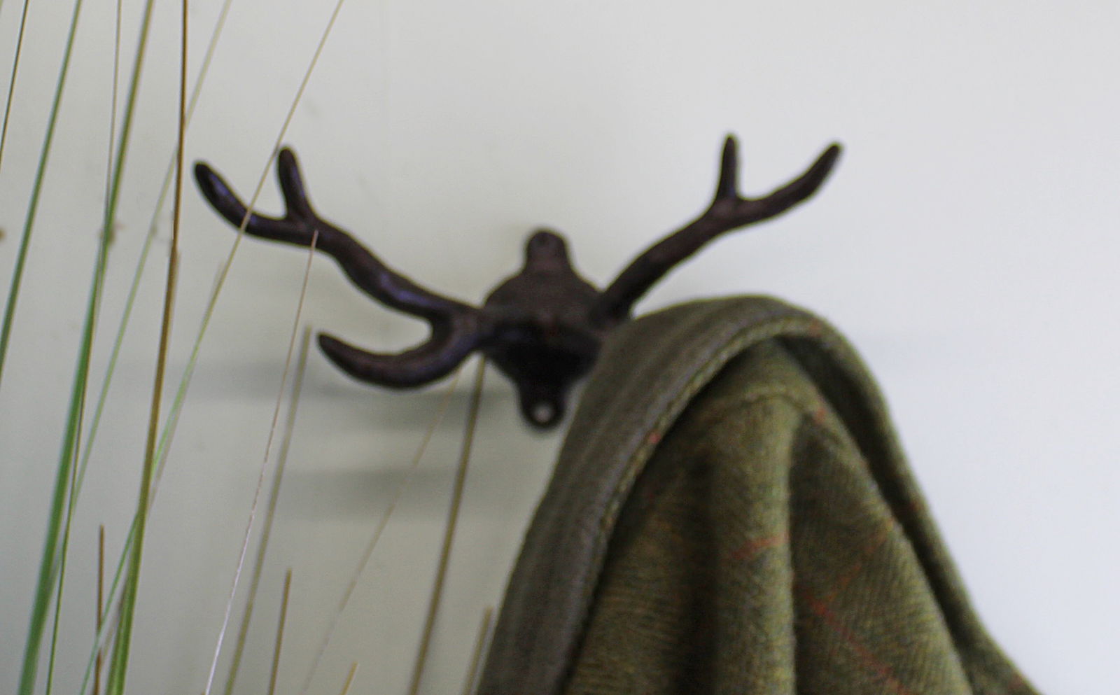 Geko Products stag antler wall mount in dark metal holding a green coat on a white wall