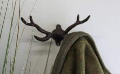 Geko Products stag antler wall mount in dark metal holding a green coat on a white wall