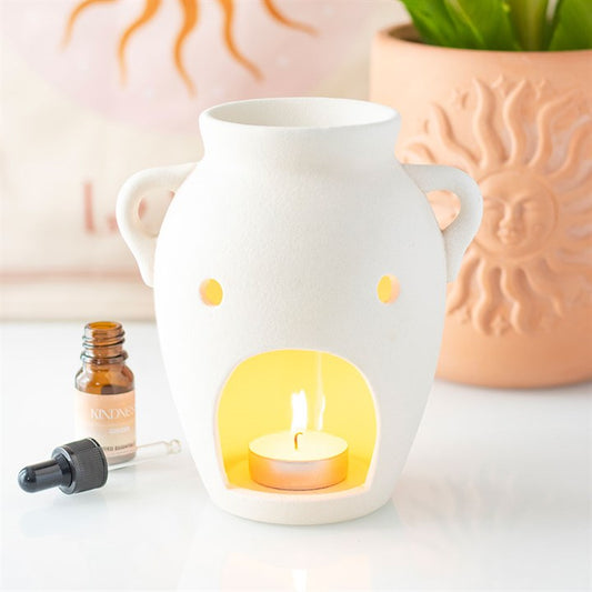 Vase shaped oil burner with tealight candle and essential oil next to decorative sun planter